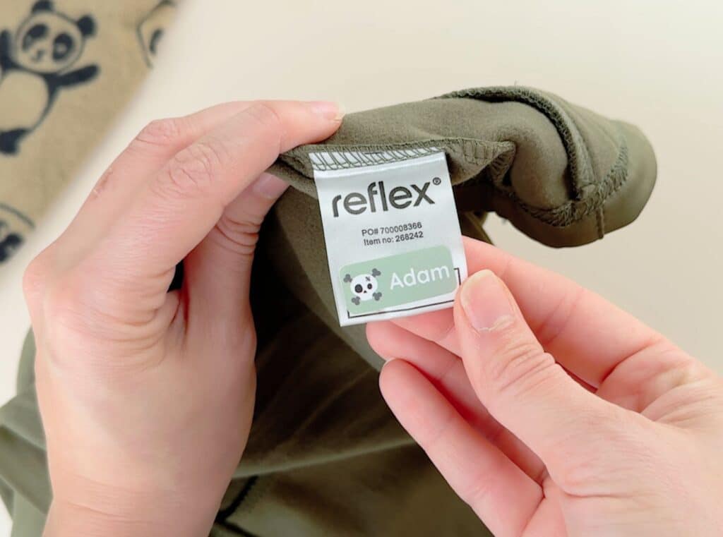 Hender som fester en grønn navnelapp på en grønn fleece bukse til barn